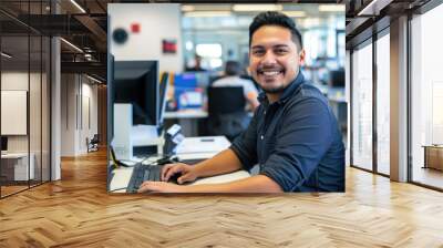 Happy and successful young latino male software engineer working at desk with computer looking front and smiling against modern office background Wall mural