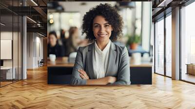 smart and smiling beautiful confident business woman smiles at the camera with crossed arms and formal wear against a modern office background Wall mural