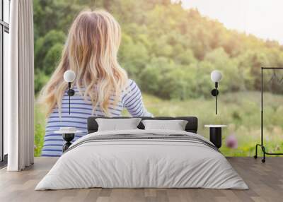 Girl sitting on a green meadow and watching the countryside landscape. Wall mural