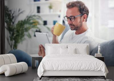 Man holding tablet, surfing online and drinking coffee. Wall mural