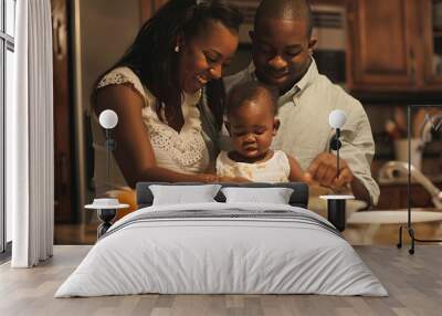 A family of three, a mother and father and a baby, are cooking together in the kitchen Wall mural