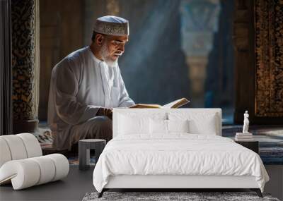 A man in a white robe is reading a book in a room with a blue carpet. The man is wearing a white hat and is sitting on the floor Wall mural