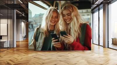 Two girls laughing on a bus. They are looking at their phones, likely sharing funny content or a funny conversation. Wall mural