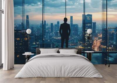 Businessman in silhouette looking out at cityscape at dusk from high rise office window Wall mural