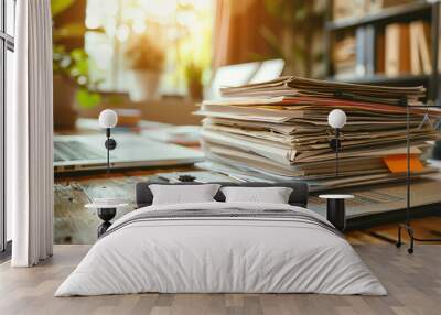 A stack of papers on a wooden desk with a laptop and a plant in the background.  The papers are organized and ready for work.  The image suggests a busy office environment. Wall mural