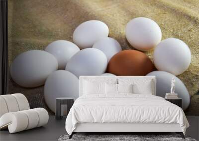 One brown egg among white eggs lies on burlap. A lone egg differs from the rest in that it stands out. The concept of leadership, the birth of an idea that is not like everyone else and standing out Wall mural