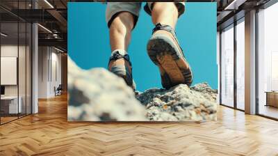 A close-up view of a hiker's feet stepping on rocky terrain with a bright blue sky above, showcasing an adventurous outdoor lifestyle. Wall mural