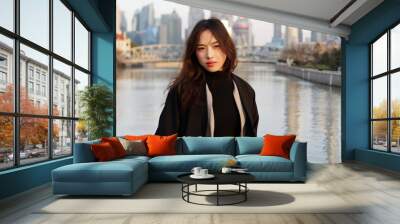 Beautiful young brunette woman in black clothes smiling at camera with  blur Shanghai Bund landmark buildings background in autumn dusk light. Emotions, people, beauty, travel and lifestyle concept. Wall mural