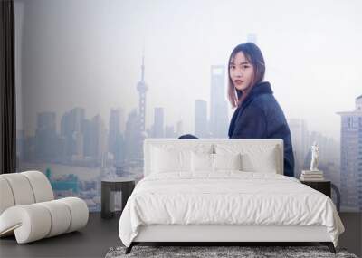 Beautiful young brunette woman sit on top of mansion roof with blur Shanghai Bund landmark buildings background. Emotions, people, beauty and lifestyle concept. Wall mural