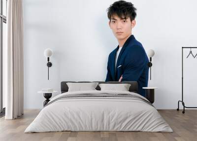 Portrait of handsome Chinese young man in dark blue leisure suit posing against white wall background. Arms crossed and looks confident. Wall mural