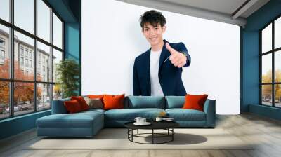 Portrait of handsome Chinese young man in dark blue leisure suit posing against white wall background. Make thumb up gesture and looks so happy. Wall mural