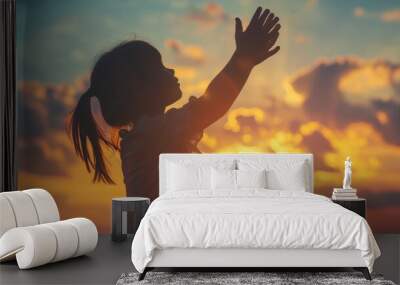 Silhouette of kid child girl raised hands worship pray. Kid girl praying in the sunset sky for a new day freedom Wall mural