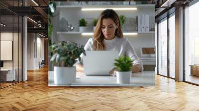 Young woman working on laptop in a modern, plant-filled home office. Cozy workspace inspiration for productivity and style. Wall mural