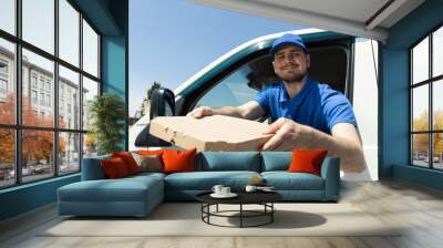 A smiling courier delivers parcels by car Wall mural