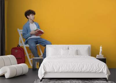 A teenager sits on a chair with a backpack and books, space for text Wall mural