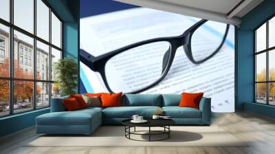 An open book with glasses on a blue background Wall mural