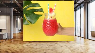 Female hand holds glass of watermelon juice on yellow background Wall mural