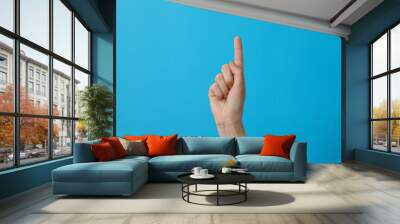 Female hand showing one finger on blue background Wall mural