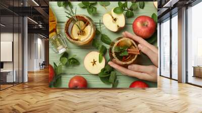 Glasses and bottle with apple cider, apples, mint and hand on green wooden background, top view Wall mural