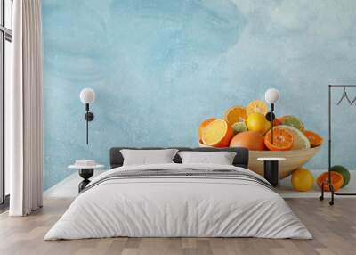 Juicy citrus fruits in bowl on wooden table against blue background, space for text Wall mural