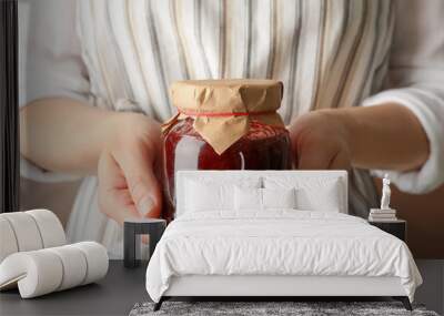 Woman holds glass jar with strawberry jam, close up Wall mural