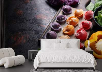 Сolored dumplings on kitchen board, pepper and basil on dark background, space for text Wall mural