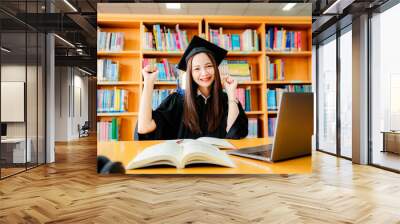 Excited Asian female university graduate celebrates successful graduation via video on laptop computer. Wall mural