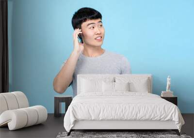 Cheerful young Asian millenial man talking on mobile phone isolated on blue studio background Wall mural