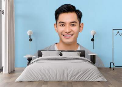 Close up portrait of happy handsome Asian man cheerfuly smiling while looking at camera in isolated studio blue background Wall mural