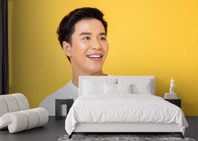 Close up portrait of young handsome Asian man cheerfully smiling and looking away in isolated studio yellow background Wall mural