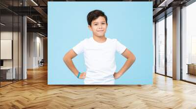 Cute mixed race boy smiling with arms akimbo in studio isolated light blue color background Wall mural