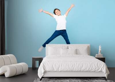 Energetic Asian mixed race boy jumping and raising hands up in isolated light blue color studio background Wall mural