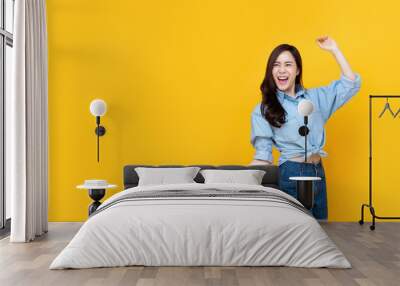 Excited pretty Asian woman smiling with arm raise Wall mural