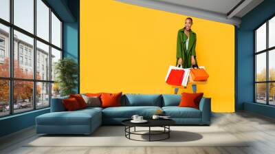 Fashionable African American woman with colorful shopping bags  isolated on yellow background Wall mural