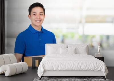 Friendly Asian delivery man  in blue polo shirt carrying parcel box Wall mural