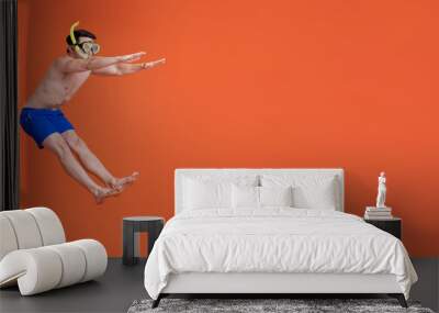 Fun happy young shirtless man wearing snorkel glasses and summer short pants jumping in isolated orange banner background Wall mural