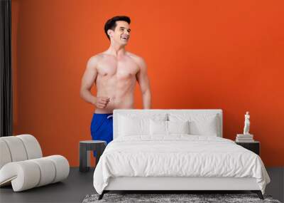 Handsome shirtless Caucasian man wearing summer short pants smiling and looking aside in colorful orange background Wall mural