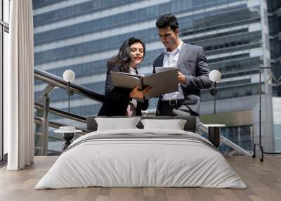 Handsome young Indian businessman in corporate wear talking with businesswoman outdoors in the city Wall mural