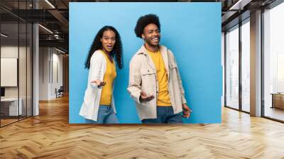 Happy smiling Afro African American couple standing with open hand gesture in light blue studio isolated background Wall mural