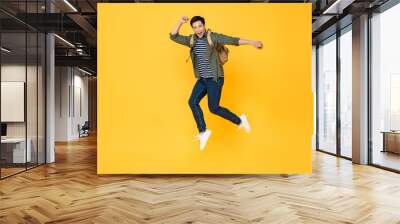 Happy smiling young Asian tourist man with backpack jumping in mid-air isolated on yellow background Wall mural