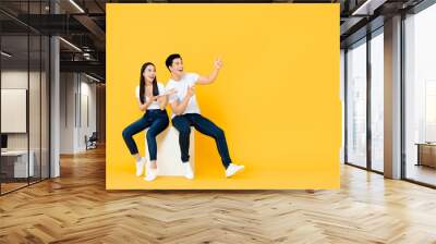 Happy surprised attractive young Asian couple pointing and looking at blank space beside in yellow isolated stuidio background Wall mural