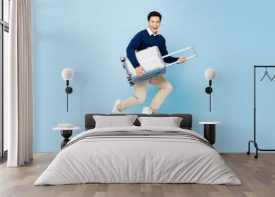 Jumping portrait of young happy smiling handsome Asian tourist man with baggage ready to travel isolated on light blue studio background Wall mural