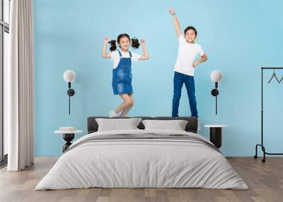 Mixed race Asian boy and girl playing by jumping in the air against light blue color isolated background studio shot Wall mural