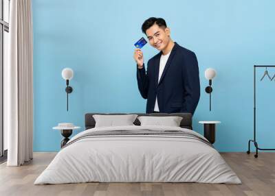 Portrait of happy handsome southeast Asian man in semi formal blazer holding credit card in light blue isolated studio background Wall mural