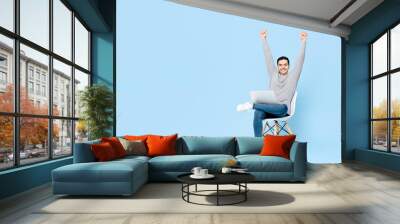 Portrait of happy young handsome Caucasian man sitting using laptop doing arms raised winning gesture in isolated studio blue background Wall mural