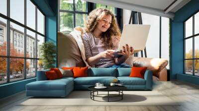 Pretty smiling Caucasian woman using laptop computer on the couch at home Wall mural