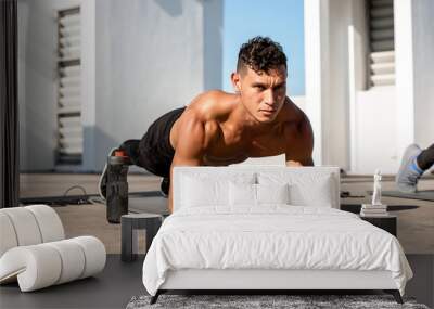 Shirtless muscular sports man doing plank workout exercise in the open air on building rooftop floor Wall mural