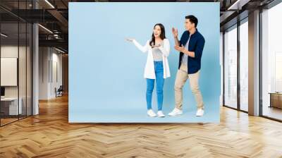 Smiling excited Asian couple tourists pointing hands to empty space aside on isolated light blue background Wall mural