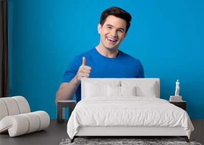 Smiling handsome young Caucasian man giving thumbs up in light blue isolated background Wall mural