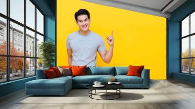 Smiling young handnsome Asian man pointing hand up to copy space aside Wall mural